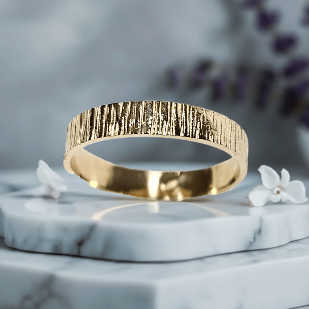 14k gold textured ring with polished finish, displayed on marble with floral background